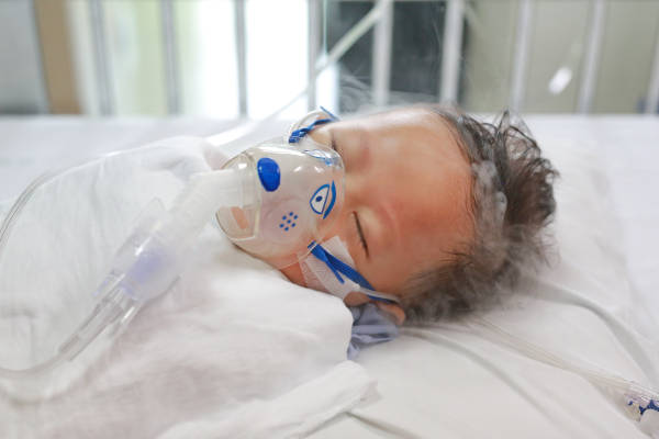 Sick baby boy applying inhale medication by inhalation mask to cure Respiratory Syncytial Virus (RSV) on patient bed at hospital.